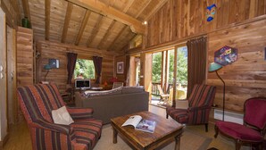 Een houten interieur met een bank, fauteuils, een salontafel en een televisie.