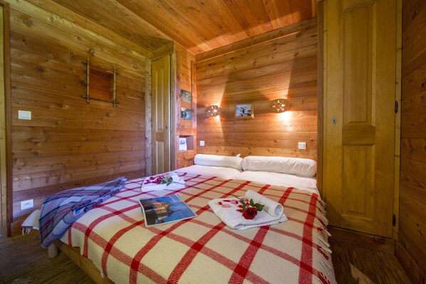 Una habitación de cabaña de madera con una cama, una puerta de madera y una lámpara pequeña en la pared.