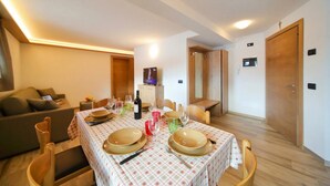 Un comedor con una mesa preparada para cuatro personas, sillas de madera, un sofá y un televisor al fondo.