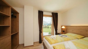 Un dormitorio con un armario de madera, una cama con ropa de cama amarilla, una mesita de noche con una lámpara y vistas a un balcón.
