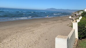 Ein Strand mit blauem Himmel, Wellen und einem fernen Gebirge.