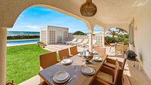 Ein Essbereich mit Meerblick, ein Pool und eine überdachte Terrasse mit Liegestühlen und einem Tisch, gedeckt für eine Mahlzeit.