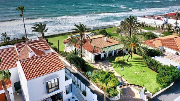 Eine Küstenwohngegend mit Häusern, deren Dächer mit roten Ziegeln gedeckt sind, Palmen und Blick auf das Meer.