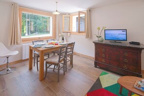 Un comedor con una mesa y sillas de madera, un televisor en una cómoda y una ventana con cortinas.