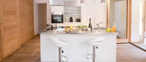 Una cocina moderna con una isla central, dos taburetes de bar, horno empotrado y cafetera.
