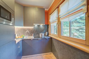 A modern kitchen with grey cabinets, a stainless steel microwave, a sink, and a window with a view of trees.