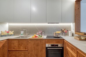 A modern kitchen with wooden cabinets, a stainless steel sink, a built-in oven, and a countertop with various kitchen items. - Androsace 31 Walk to Ski Lifts + Pool & Mont-Blanc View in Argentière, Argentière (Chamonix), France (Argentière (Chamonix))