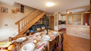 A dining area with a wooden table set for four, a staircase, a kitchen, and a living room with a sofa. - Azalea, Livigno, Italy (Livigno)