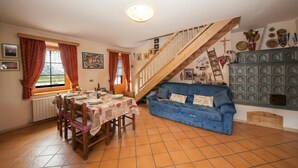 A dining area with a table set for four, a blue sofa, a wooden staircase, and a wall with decorative plates and a cross. - Azalea, Livigno, Italy (Livigno)