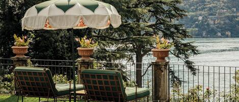 Une terrasse avec deux fauteuils et un parasol vert, donnant sur un lac avec des bâtiments en arrière-plan.