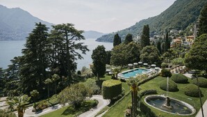 A resort with a swimming pool surrounded by manicured gardens, a lake, and mountains in the background. - Passalacqua (Moltrasio)