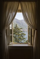 Une fenêtre avec des rideaux blancs, une vue sur un lac et, au loin, une montagne couverte de forêts.