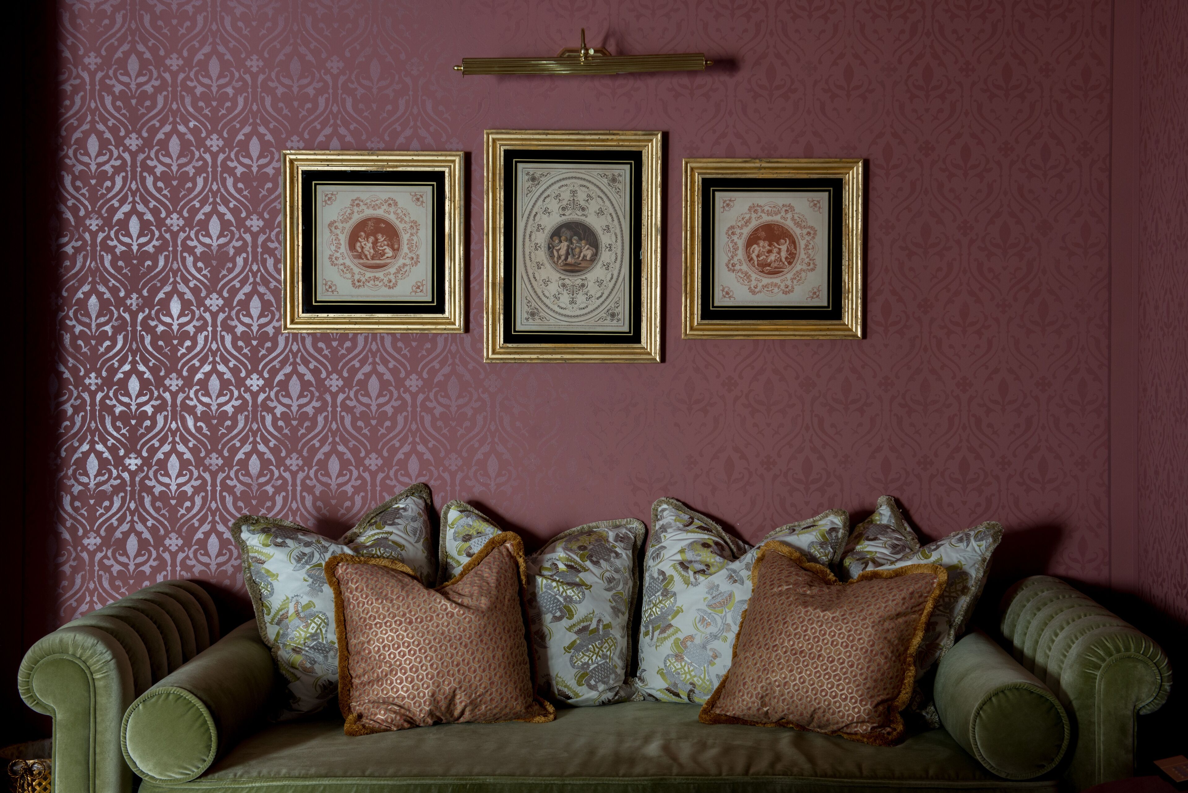 A green sofa with patterned cushions against a wall with framed artwork.