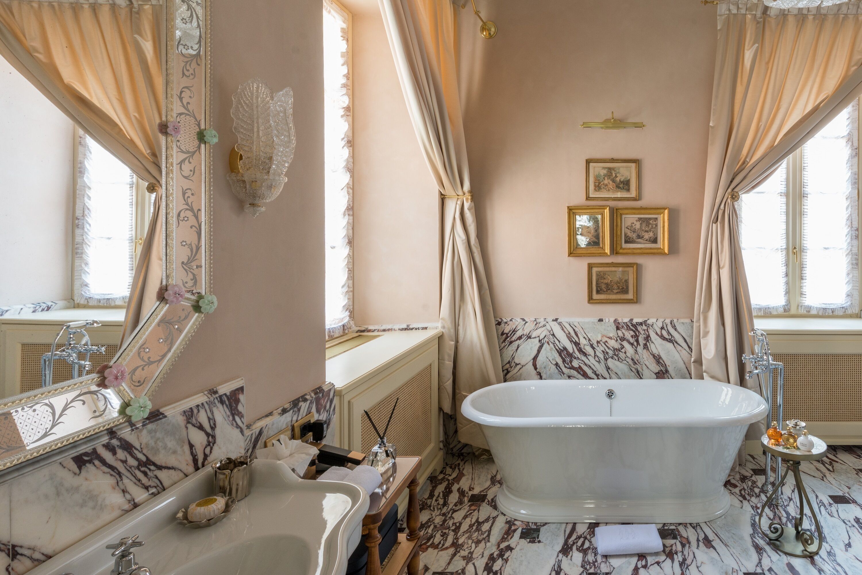 A classic bathroom with a freestanding bathtub, marble walls, and a large mirror with floral decorations.