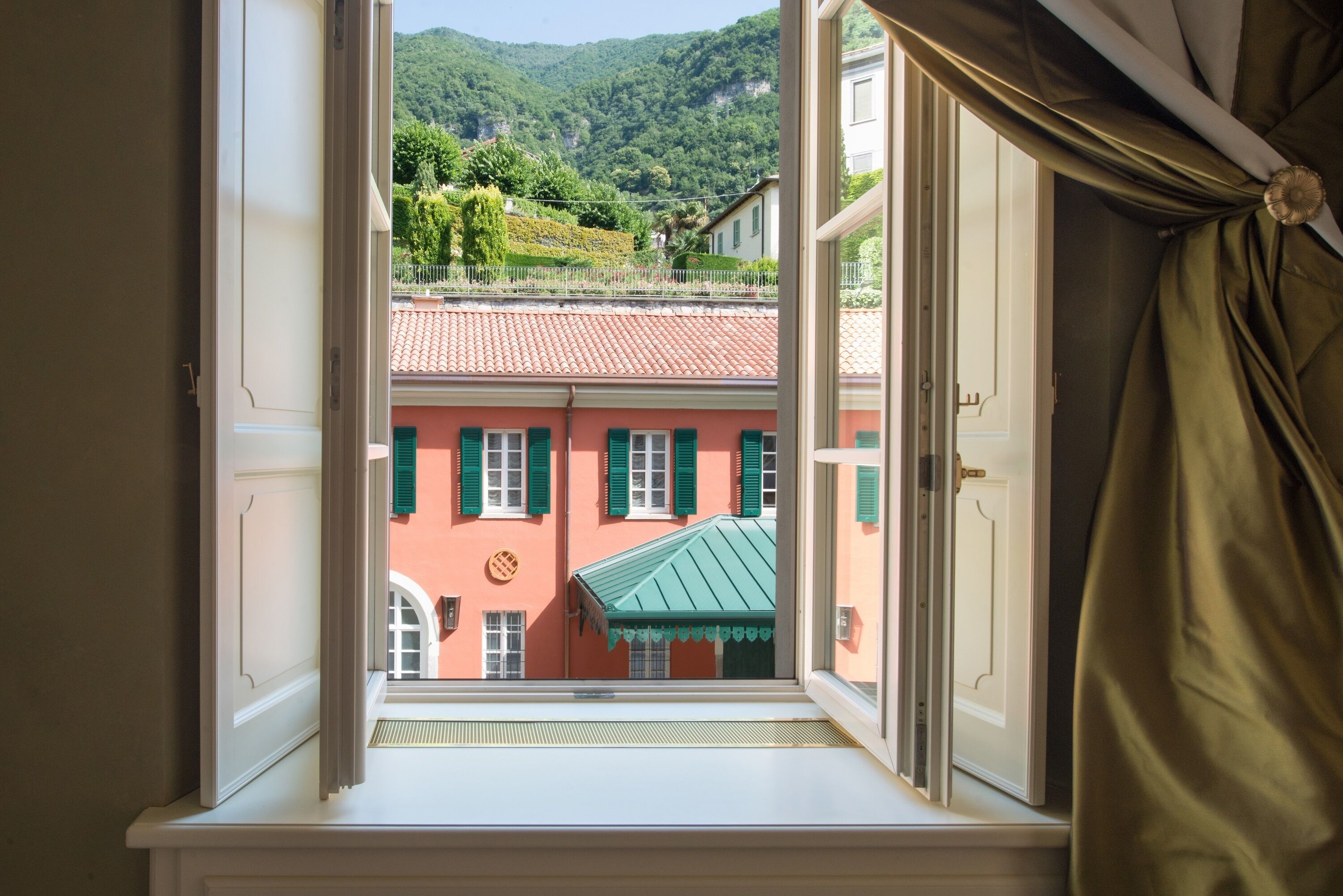 A window with a view of a building with a red roof and green shutters.