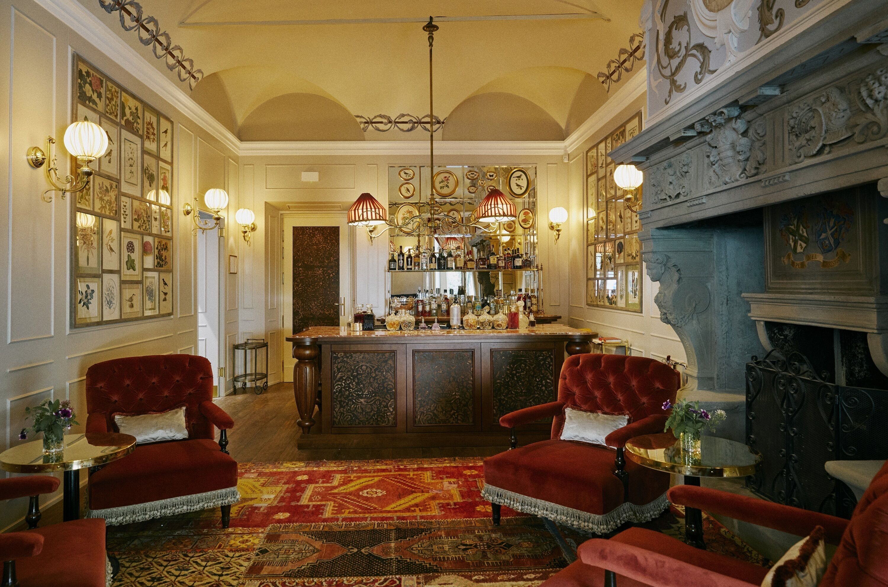 A bar area with red velvet chairs, a patterned rug, and a bar stocked with bottles.