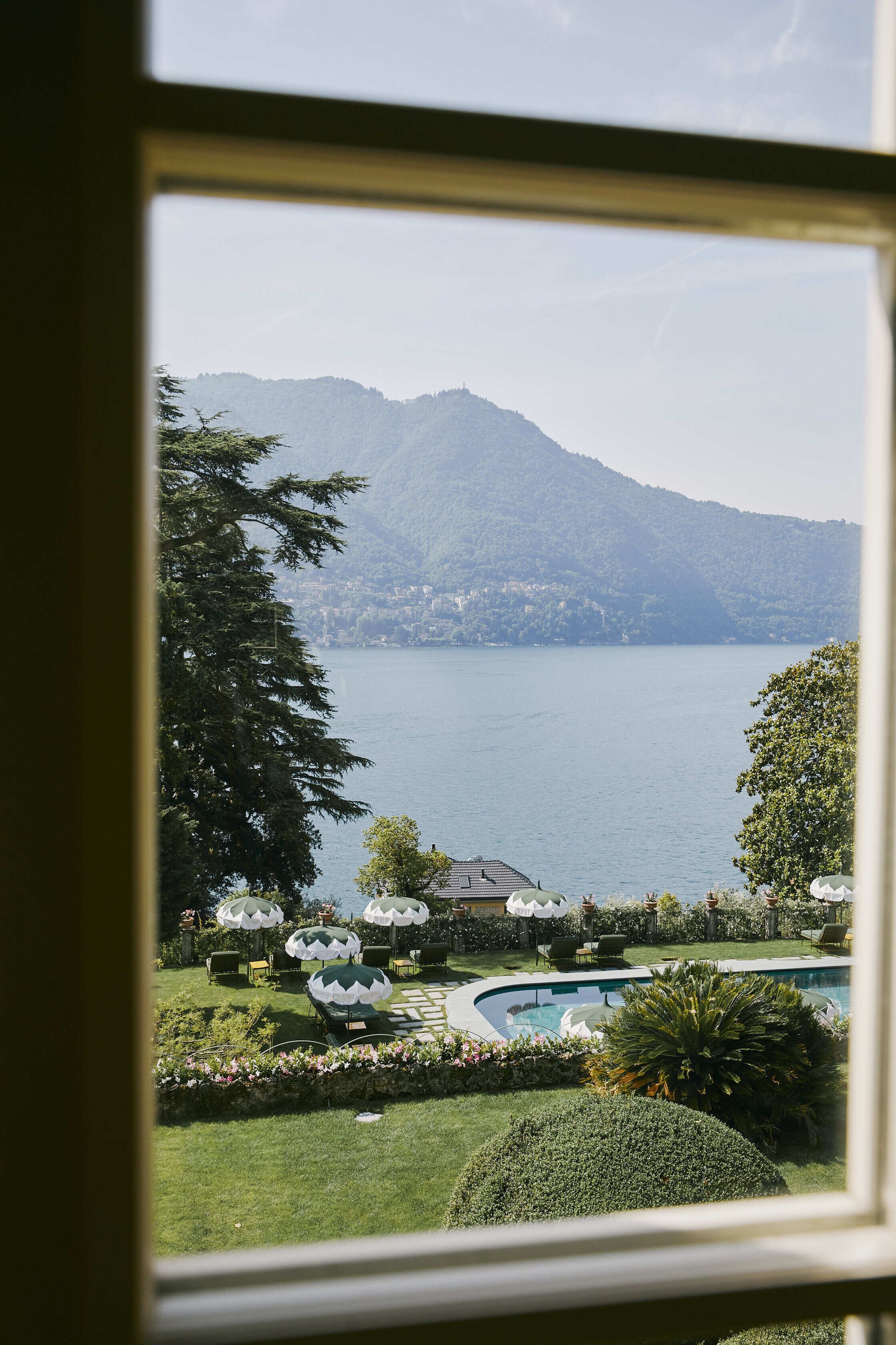 A view of a lake with mountains in the background, a swimming pool, and outdoor umbrellas.