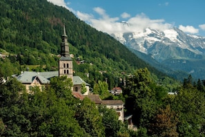 A church with a tower, surrounded by forested mountains and snow-capped peaks. - St. Gervais - Le Bois des Fées 2, Saint Gervais Les Bains (Chamonix), France (Saint Gervais Les Bains (Chamonix))