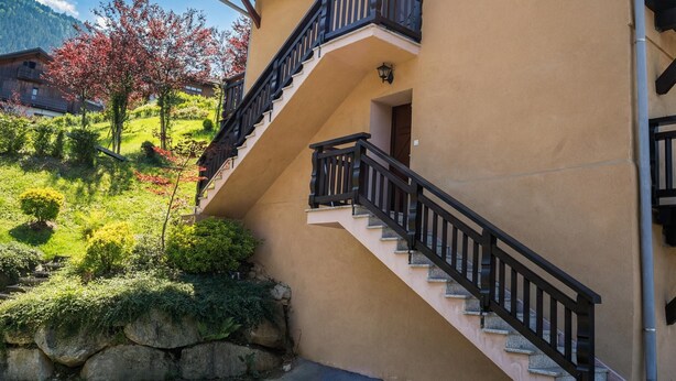 Un bâtiment à la façade beige, avec un escalier noir doté d’une rampe et un mur en pierre.