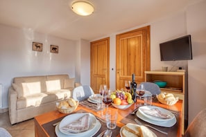 Un coin repas avec une table dressée pour deux personnes, un canapé, des meubles en bois et un téléviseur fixé au mur.