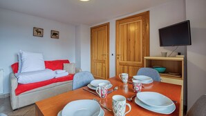 Un coin repas avec une table en bois dressée pour quatre personnes, un canapé rouge et blanc, et deux portes en bois.