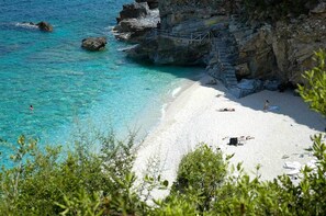 Une plage à l’eau turquoise et limpide, bordée de falaises rocheuses, où quelques personnes se prélassent au soleil.