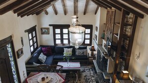 A cozy room with a dark blue sofa, a wooden ceiling, and a hanging light fixture. - PELION HOMES | STONE HOUSE  charming villa with amazing view for 2-4 guests (Agios Georgios Nilias)