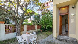 Une terrasse extérieure avec une table et des chaises, un arbre et l’entrée d’un bâtiment.
