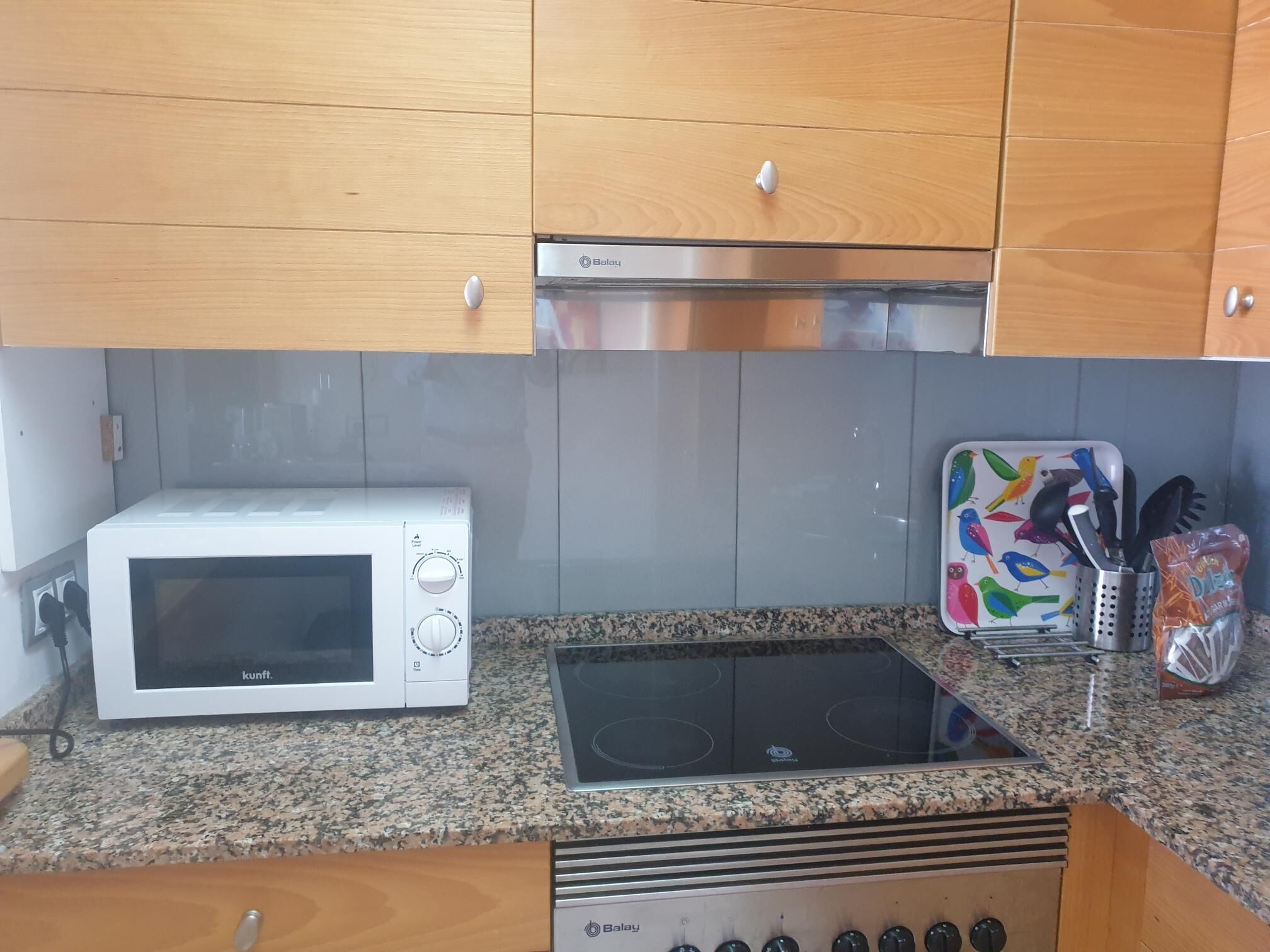 A kitchen with a white microwave, a stove, and a colorful bird-themed toaster.