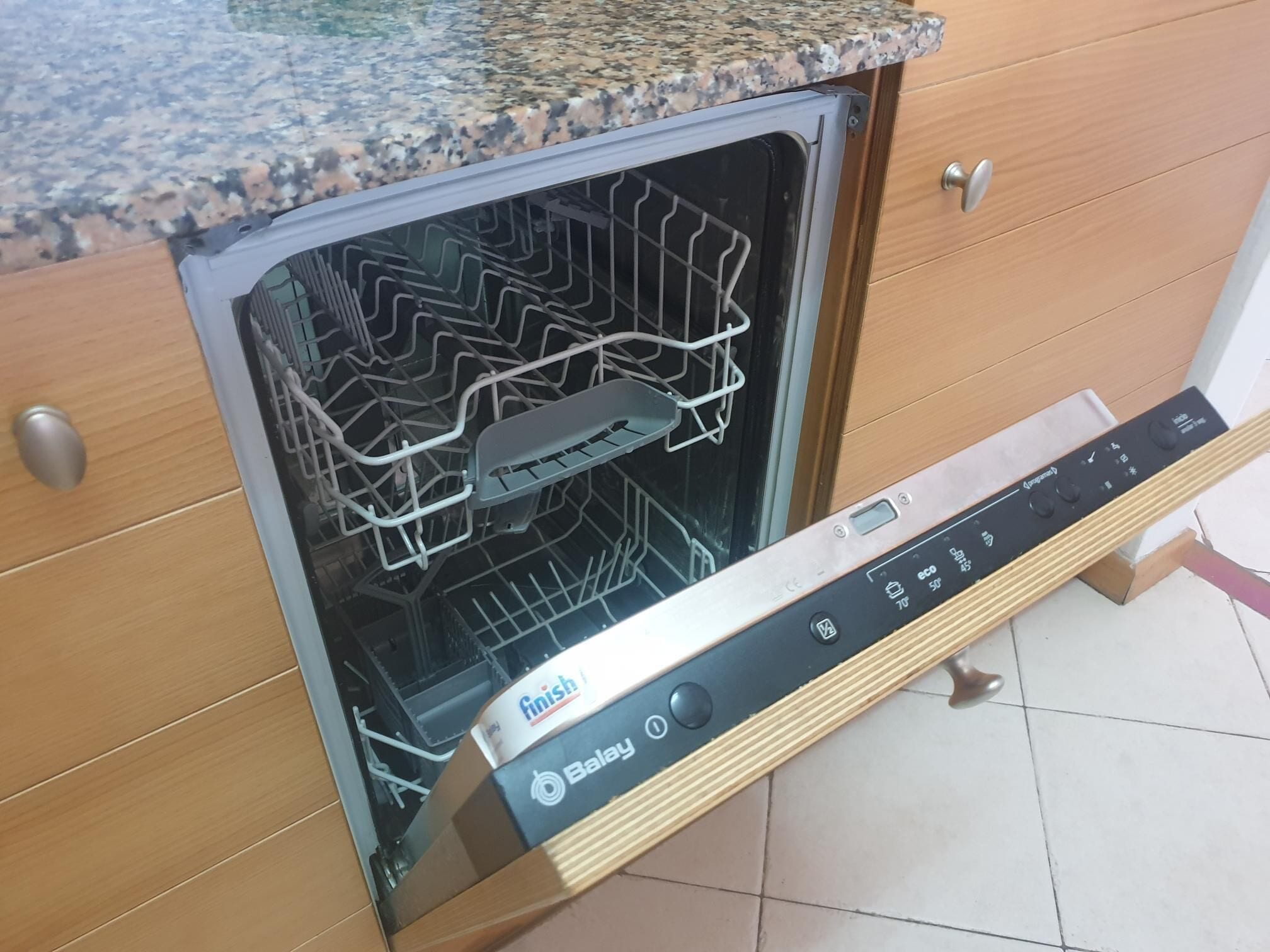 Un lavavajillas con panel de control, ubicado en una cocina con armarios de madera y encimera de granito.