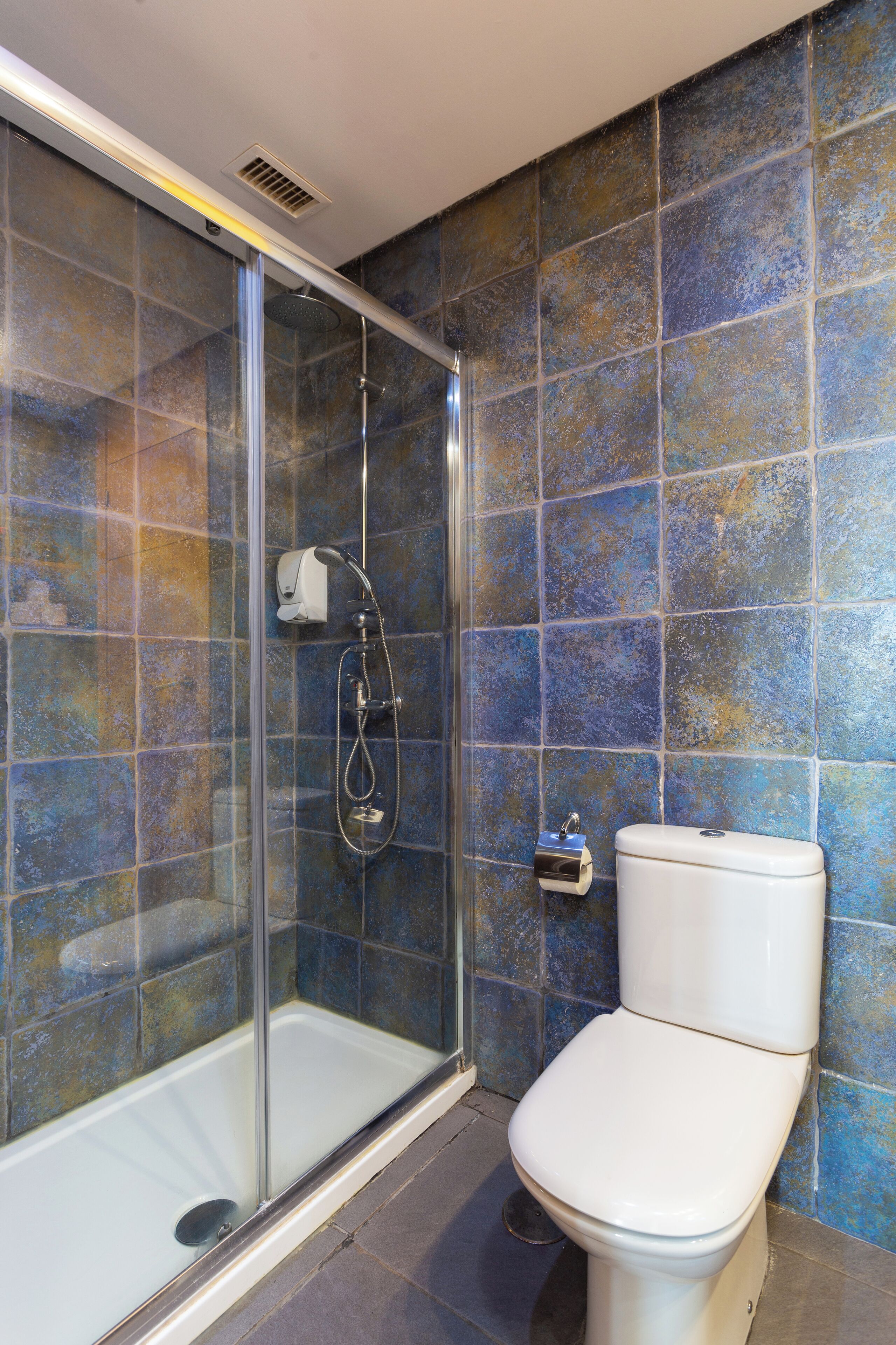 Un baño con ducha de vidrio, inodoro y paredes con azulejos.