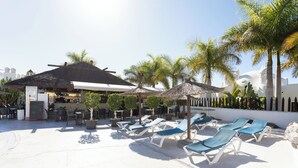 A poolside area with sun loungers, palm trees, and a bar area. - Incredible villa in urbanization with heated pool (Adeje)