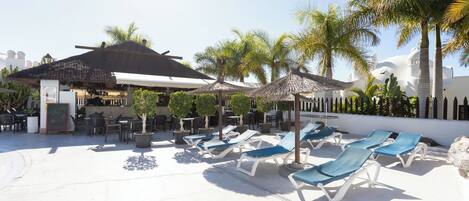 A poolside area with sun loungers, palm trees, and a bar area.