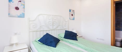 Une chambre double avec deux lits, une table de chevet blanche, une lampe fixée au mur et deux tableaux représentant des fleurs.