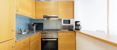 Une cuisine compacte avec des meubles en bois, un four à micro-ondes, une cuisinière et une machine à café.