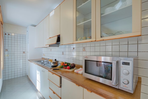 A kitchen with white cabinets, a stainless steel microwave, and a tiled backsplash. - Rododendro, Livigno, Italy (Livigno)