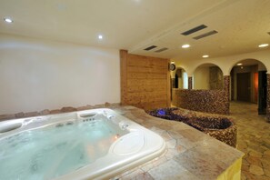 A spa area with a hot tub, stone flooring, wooden paneling, and a tiled wall. - Rododendro, Livigno, Italy (Livigno)