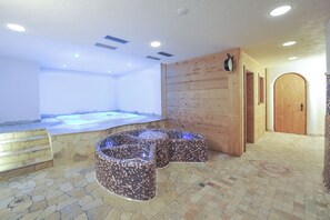 Ein Wellnessbereich mit Whirlpool, Mosaik Sitzgelegenheiten, Steinstufen und Holzwänden.