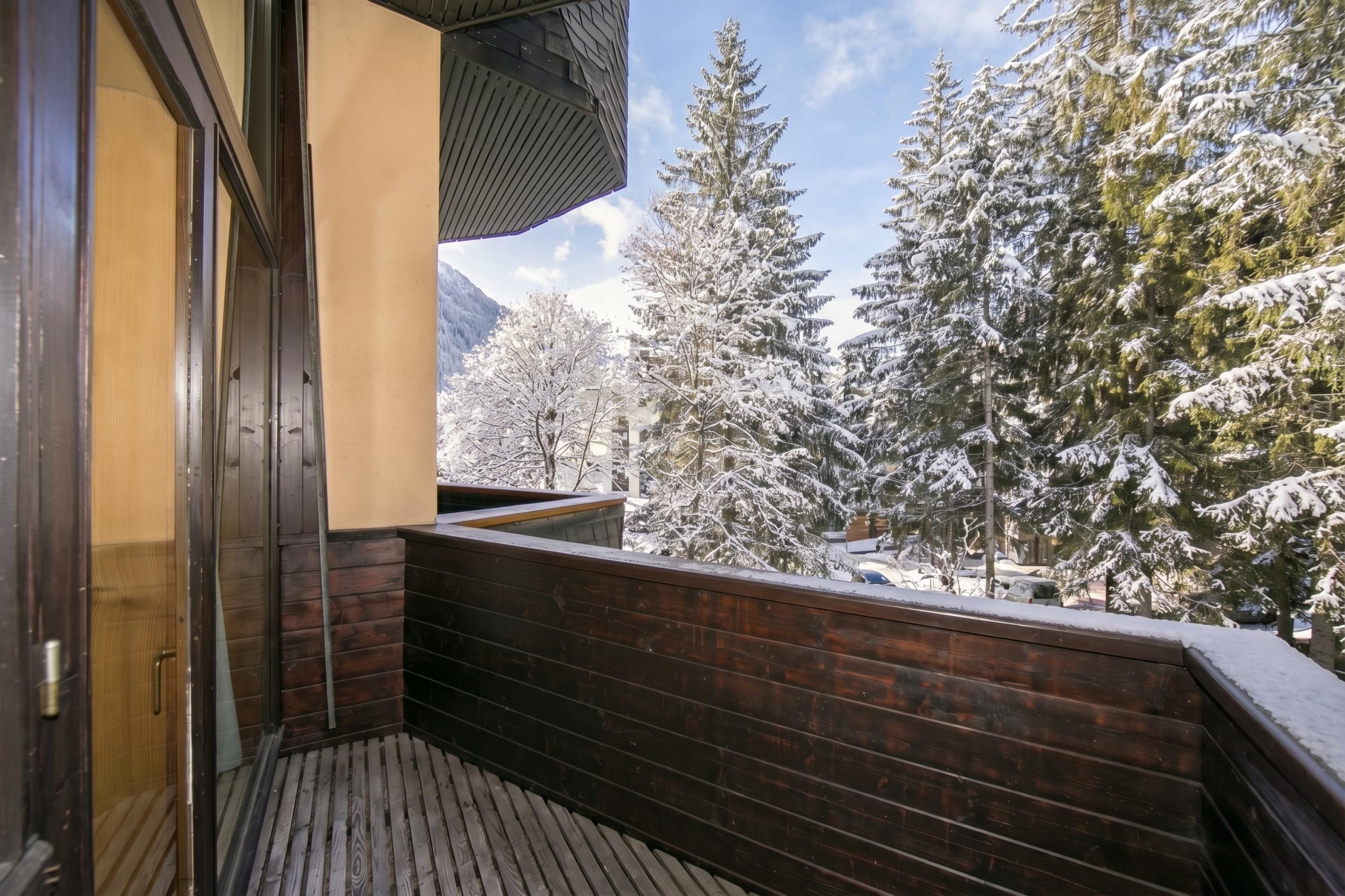 Un balcon en bois offrant une vue sur des arbres couverts de neige et une montagne en arrière-plan.