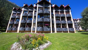 Un hôtel à plusieurs étages doté de balcons, d’un jardin fleuri et surplombant un paysage montagneux.