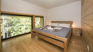 Une chambre avec un lit en bois, une table de chevet, une fenêtre donnant sur des arbres et un mur en bois.