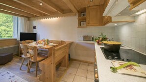 Un intérieur en bois comprenant une table à manger, des chaises, un téléviseur, un coin cuisine avec une cuisinière et une fenêtre avec des rideaux.