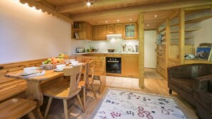Un intérieur en bois comprenant une table à manger, des chaises, un canapé et un coin cuisine avec des placards et des appareils électroménagers.