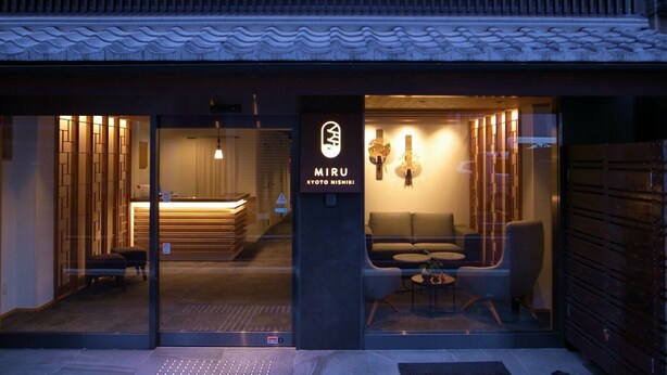 Een hotelingang met een receptiebalie, een zithoek en een bord waarop 'MIRU KYOTO NISHIKI' staat.