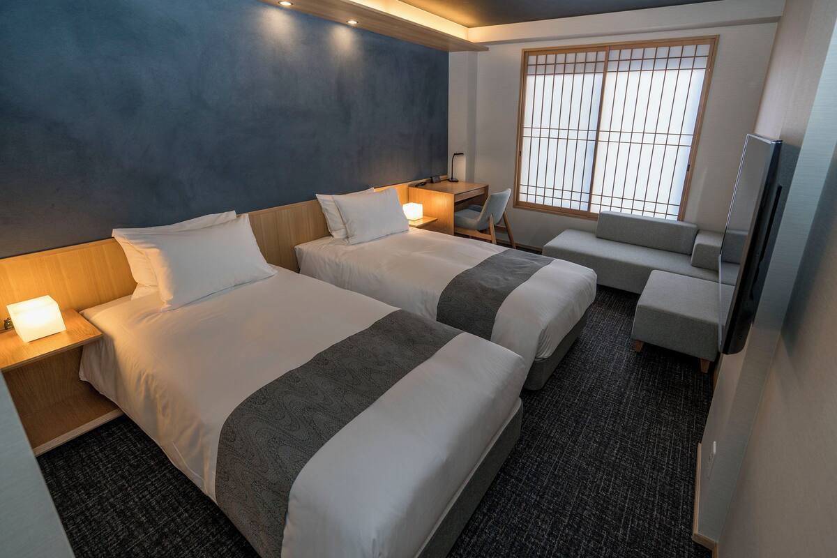 Une chambre d’hôtel avec deux lits, un bureau, une chaise, une télévision et une fenêtre donnant sur un beau paysage.