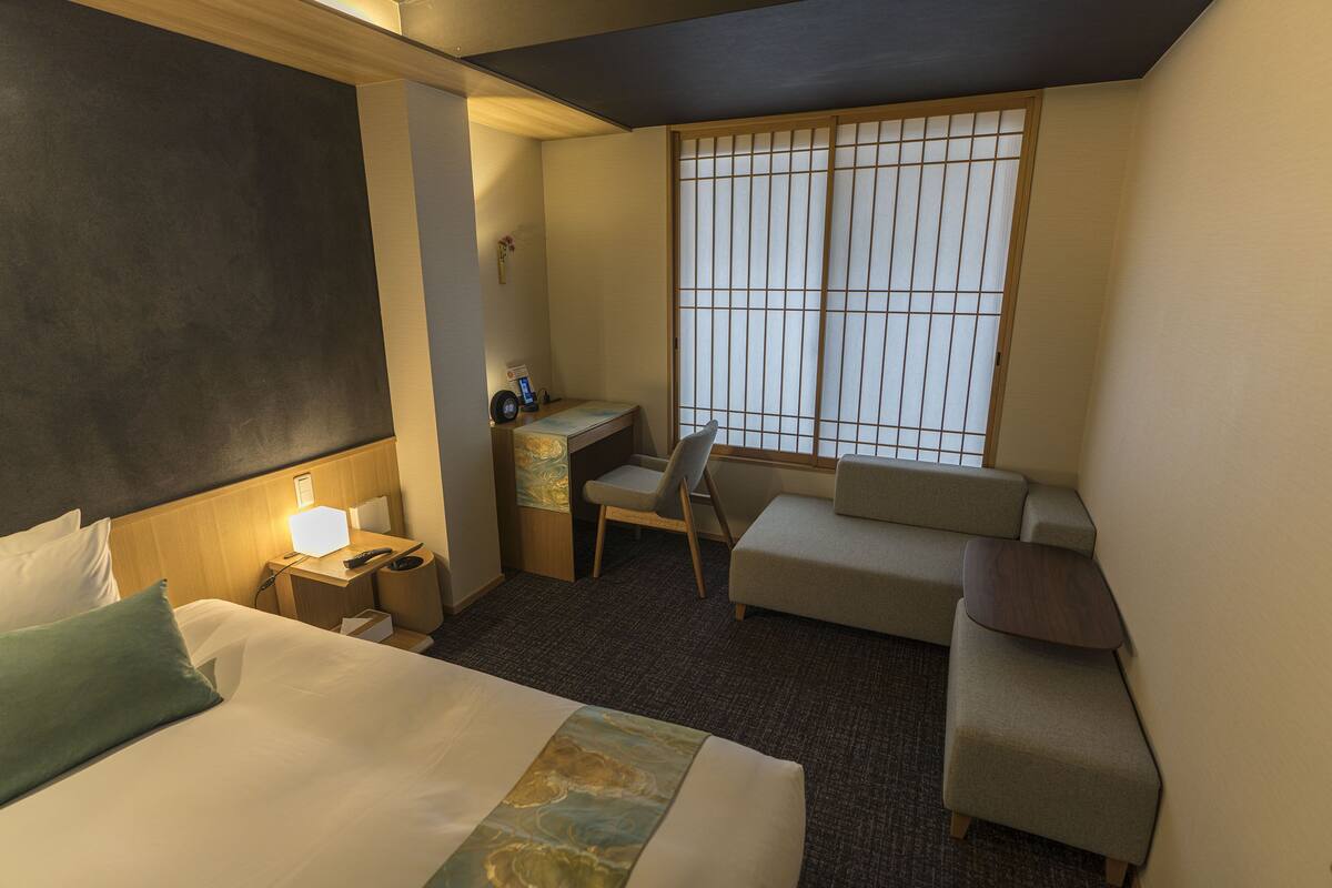 Une chambre d’hôtel avec un lit, un bureau, une chaise, un canapé et une fenêtre donnant sur un beau paysage.