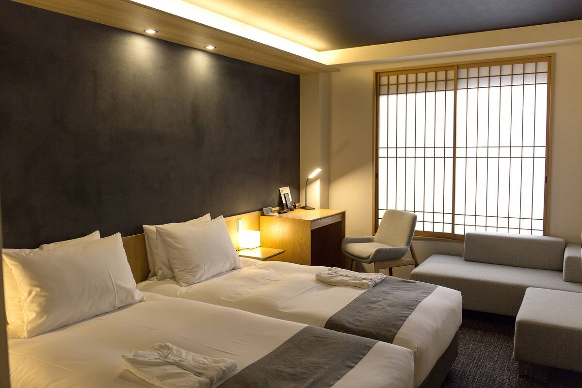 Une chambre d’hôtel avec deux lits, un bureau, une chaise et un canapé.