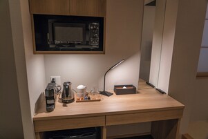 Un kitchenette pequeño con microondas, cafetera y un mueble bajo.