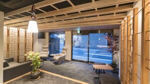 Een moderne receptie met een houten plafond, een receptiebalie, zitplaatsen en uitzicht op de straat door glazen deuren.