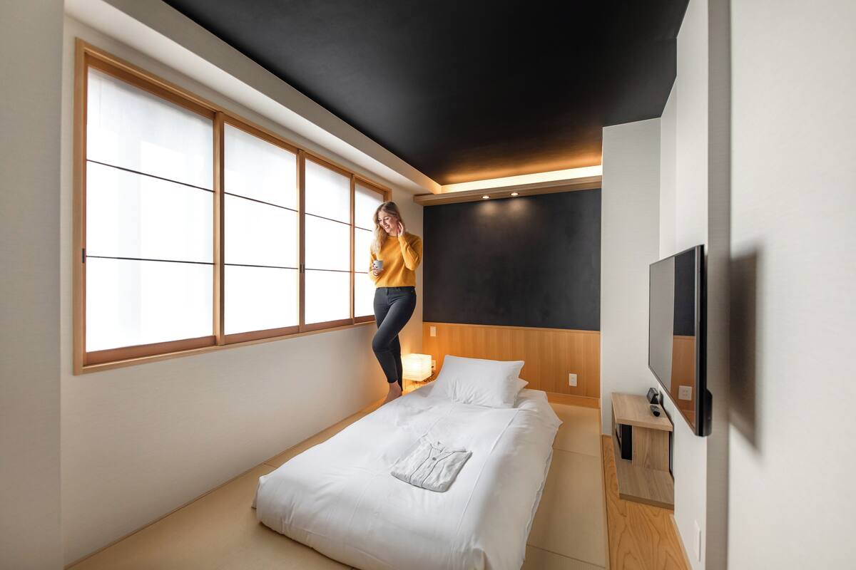 Une chambre à coucher moderne avec une grande fenêtre, un lit, une télévision et une table de chevet.